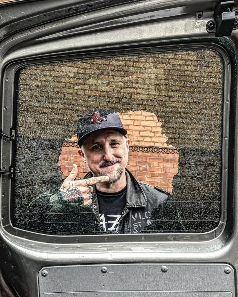 Jane’s Addiction, guitar and bass tech Dan Cleary stands beside a van window broken by Dave Navarro’s pedalboard.